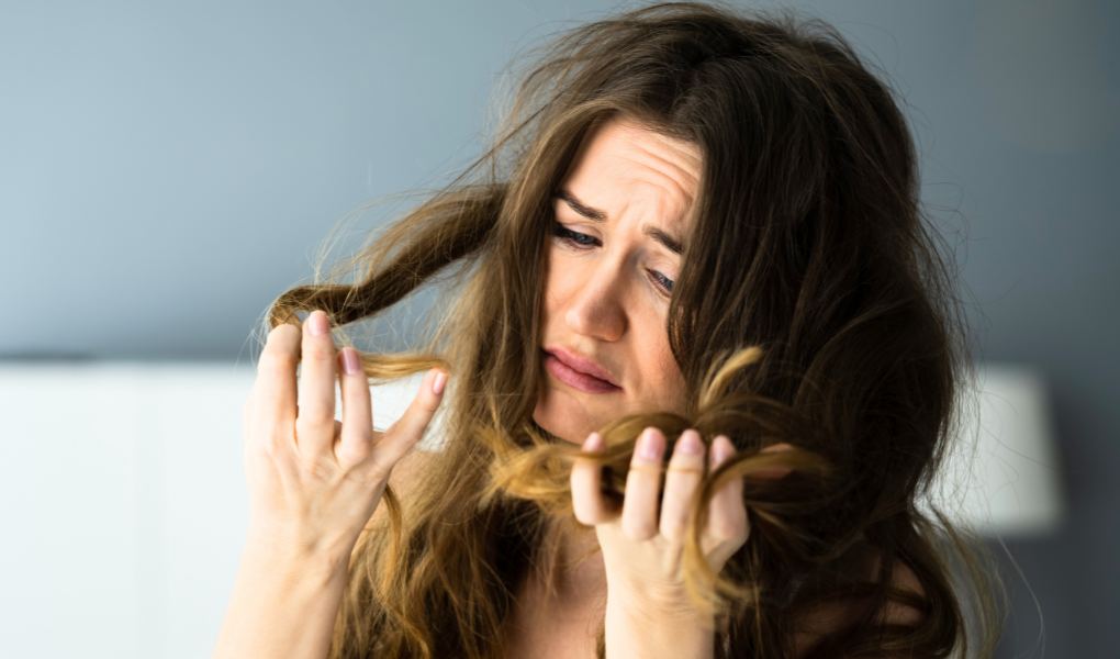 Woman with long brown hair looking at the split ends and appearing frustrated