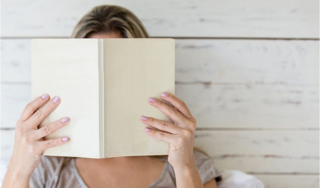 Woman reading a book, with her face hidden behind the book